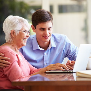 young man assisting senior woman with laptop